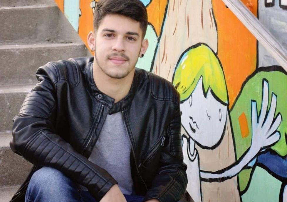 Vitor Abreu sentado em uma escada de concreto, com uma parede ao seu lado com desenhos feitos em grafite