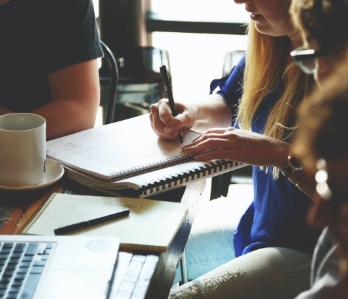 Estudantes sentados a mesa anotando seus estudos em um caderno
